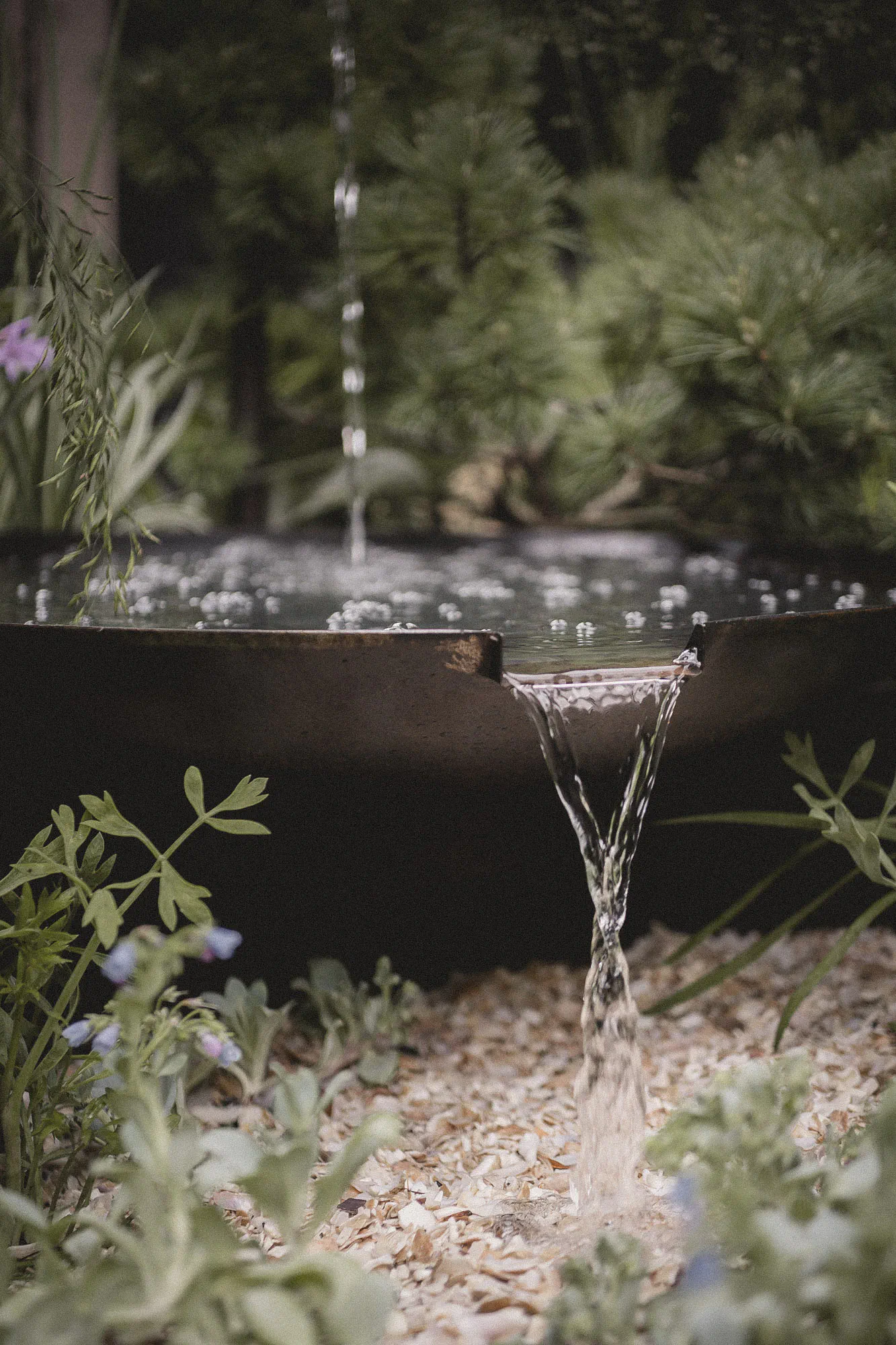 Water spilling from a notch in a dark steel bowl onto crushed shells